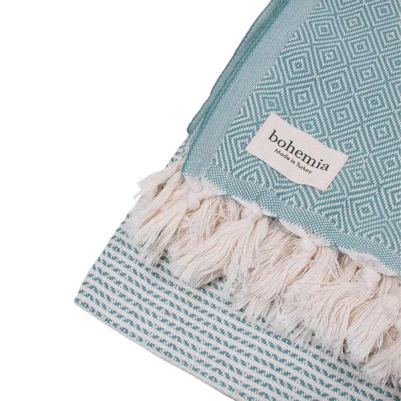 A cotton towel in a mint color with an intricate design and white fringe.