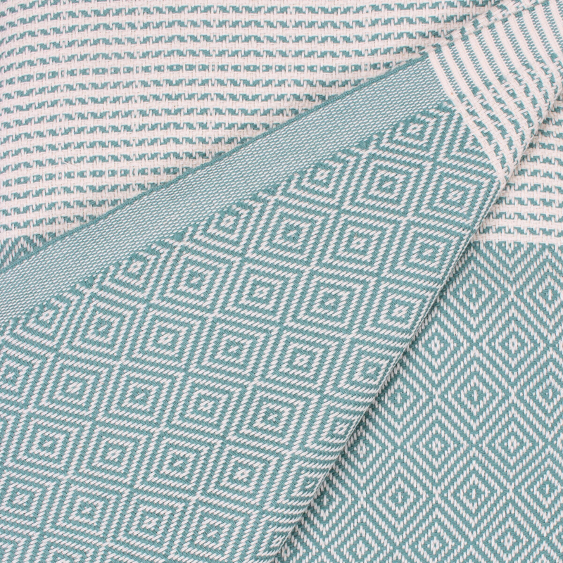 A cotton towel in a mint color with an intricate design and white fringe.