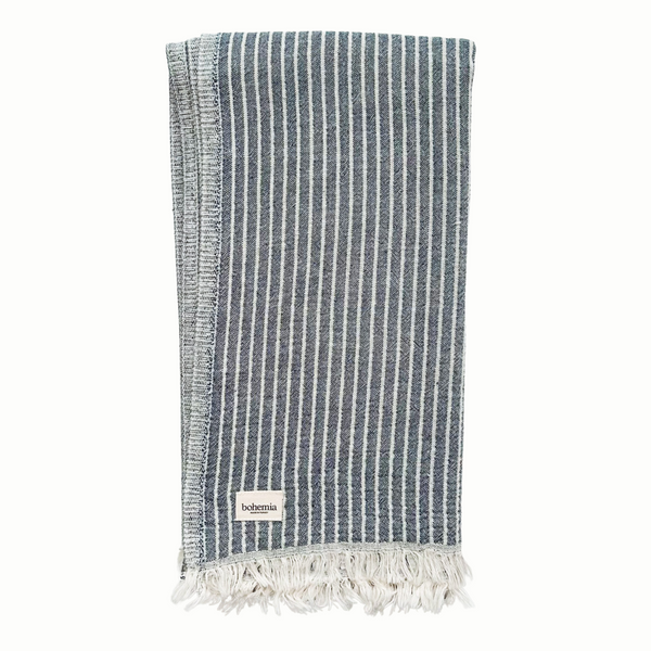 A cotton towel in an indigo color and subtle striped pattern with a white fringe.