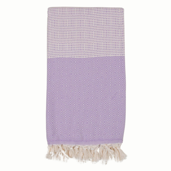 A cotton towel in a lavender color with an intricate design and white fringe.