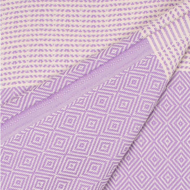 A cotton towel in a lavender color with an intricate design and white fringe.