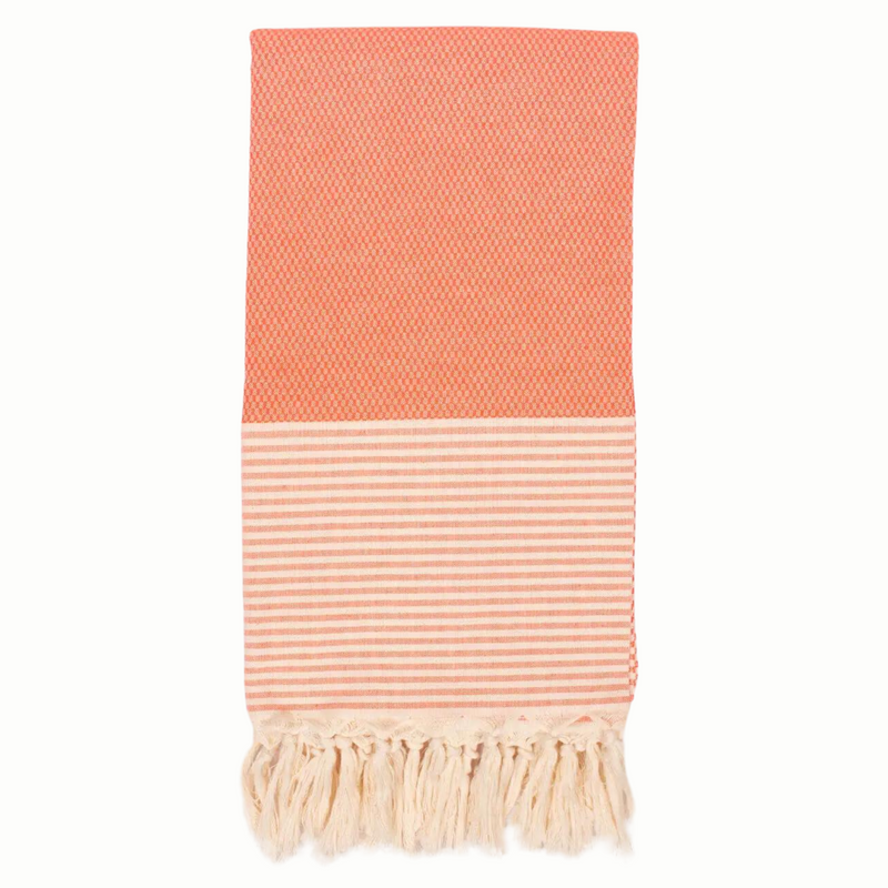 A cotton towel in an orange color with a subtle striped pattern and white fringe.