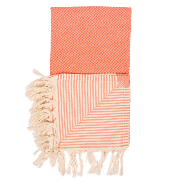 A cotton towel in an orange color with a subtle striped pattern and white fringe.