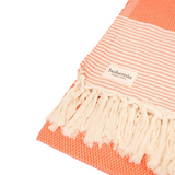 A cotton towel in an orange color with a subtle striped pattern and white fringe.