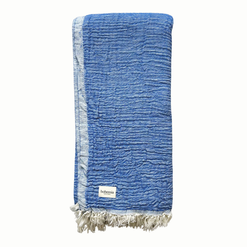 A cotton muslin towel in a rich blue color with a white fringe.