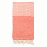 A cotton towel in a tangerine color with an intricate design and white fringe.