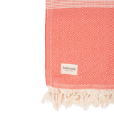 A cotton towel in a tangerine color with an intricate design and white fringe.