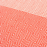 A cotton towel in a tangerine color with an intricate design and white fringe.