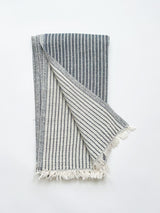 A cotton towel in an indigo color and subtle striped pattern with a white fringe.