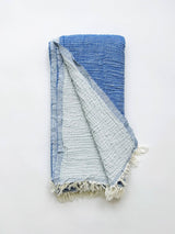 A cotton muslin towel in a rich blue color with a white fringe.