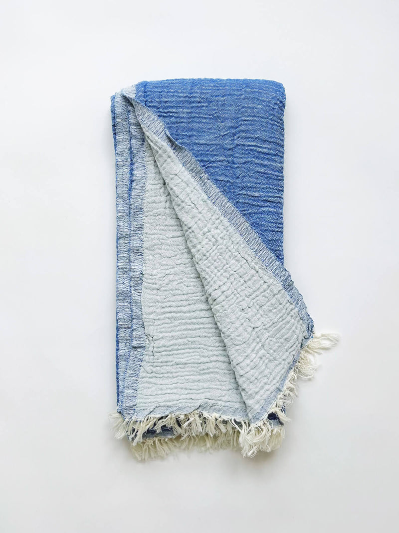 A cotton muslin towel in a rich blue color with a white fringe.